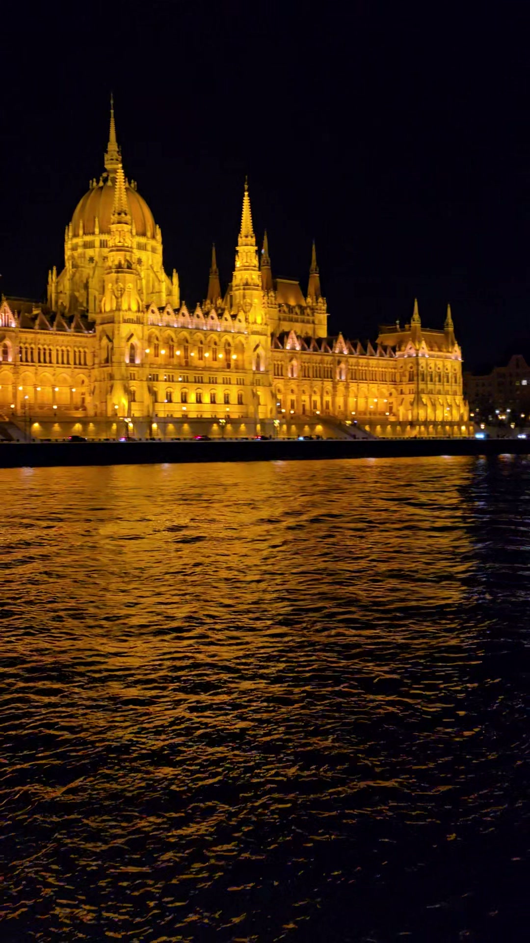 The Hungarian Parliament Building illuminated in gold at night, reflected in the Danube, seen from the river